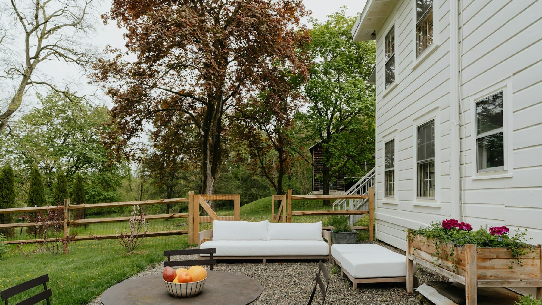 Backyard patio with white outdoor sofas and a round table beside a white house