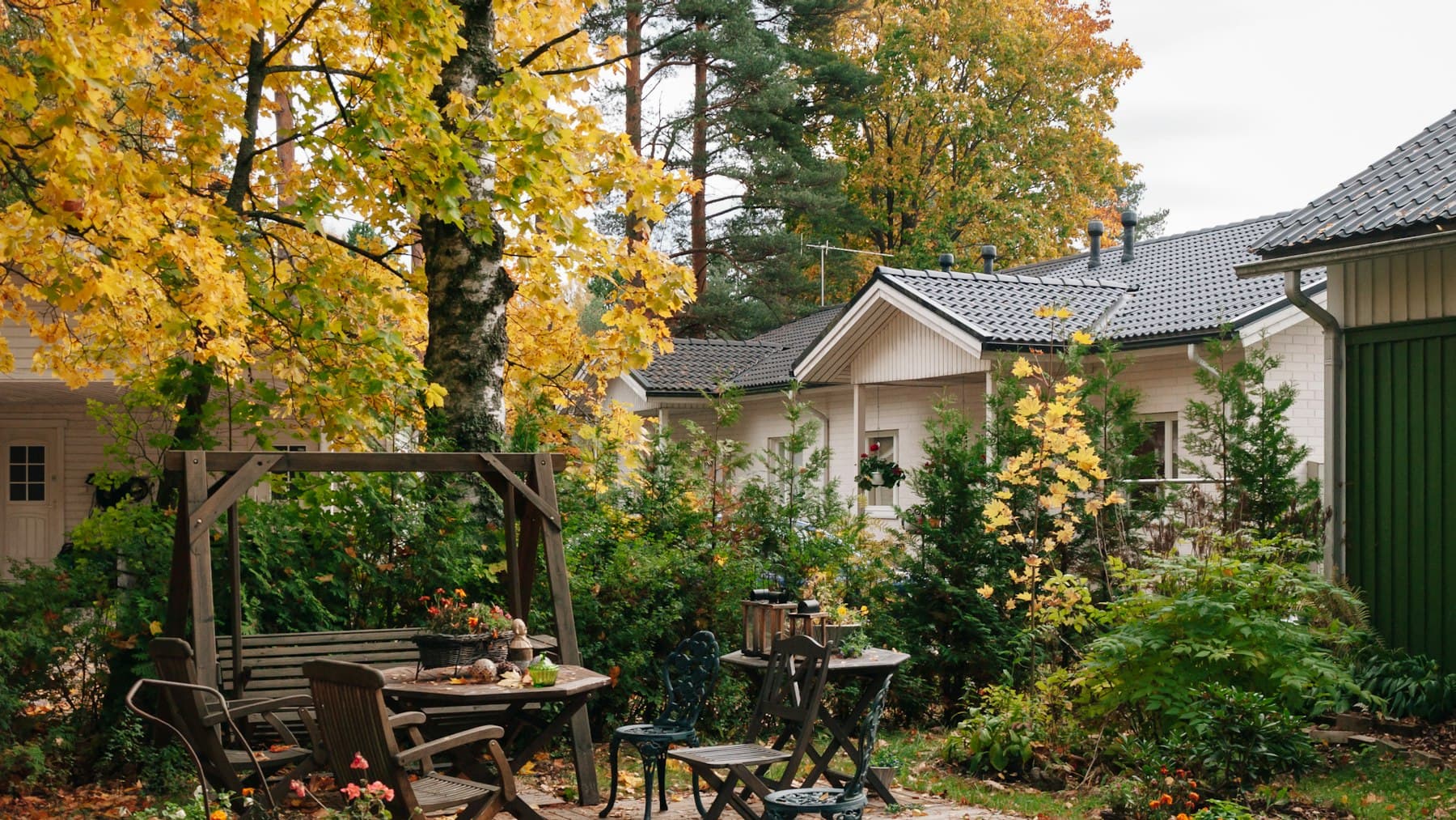 Landscaped backyard with a dining table, swing, and colorful trees beside a home