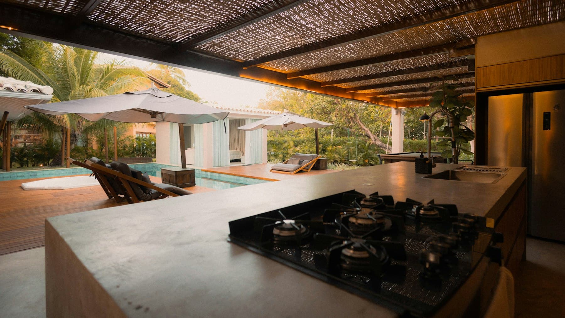 Covered outdoor kitchen with a gas cooktop and counter overlooking a pool