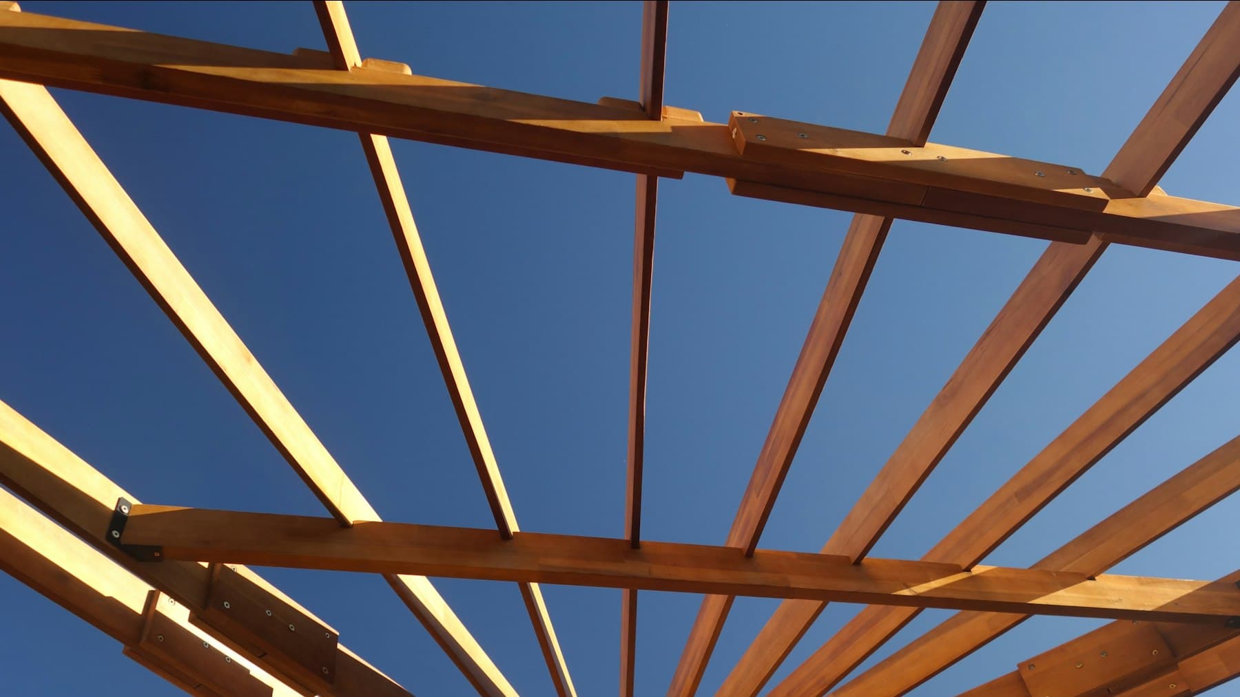 Looking up through the beams of a wood pergola with integrated lighting at dusk