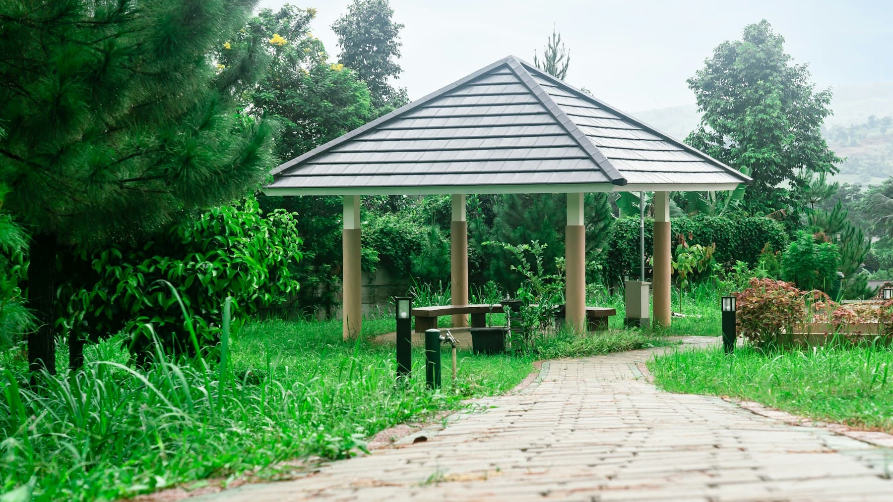 Gazebo with a solid roof standing in a green park, compared with an open pergola