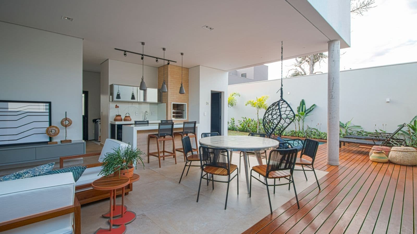 Covered patio outdoor kitchen bar with counter seating, pendant lights and dining set opening onto a wood deck and garden