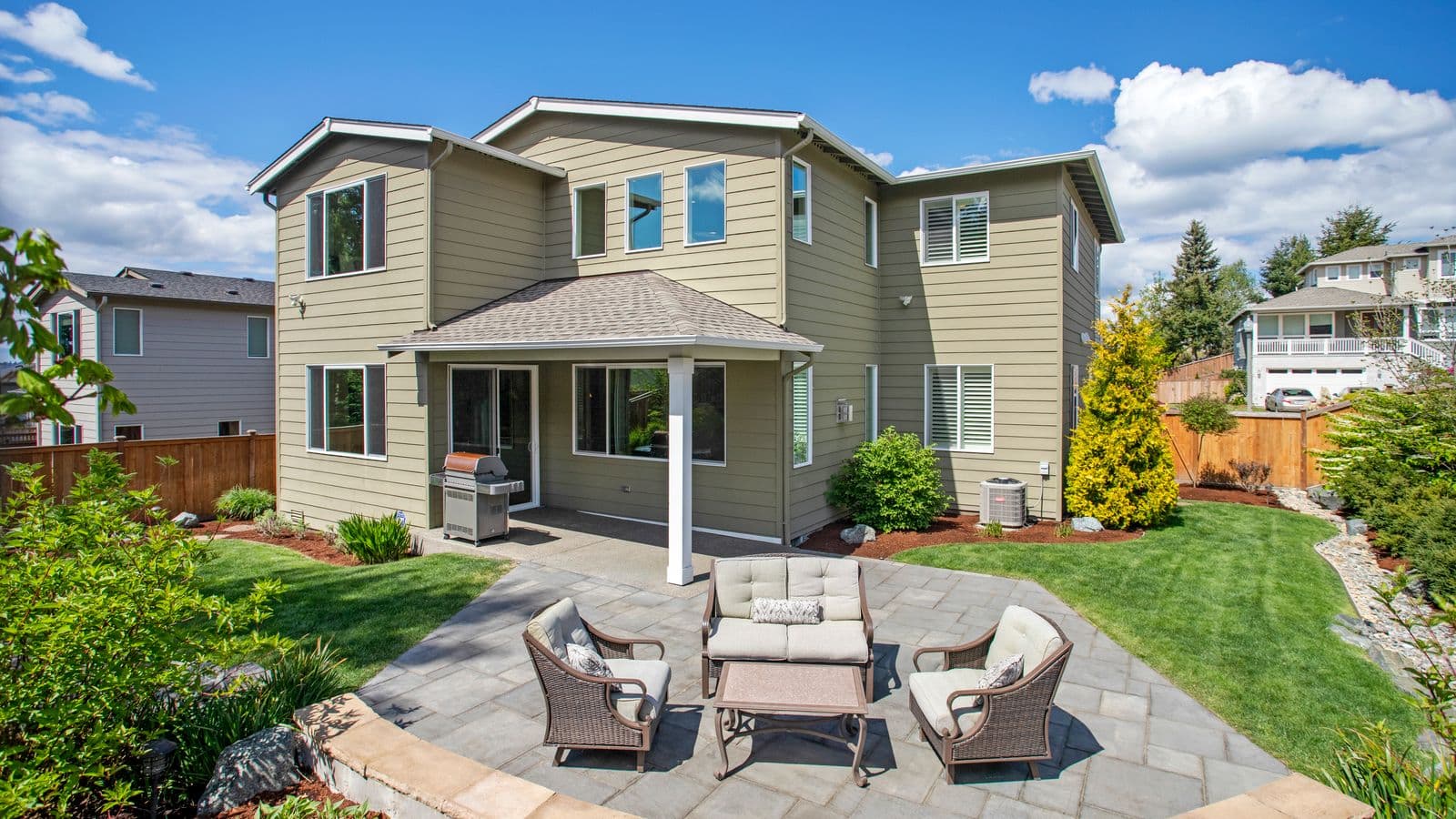 Curved bluestone paver patio with cushioned outdoor lounge furniture bordered by a manicured lawn under a clear blue sky