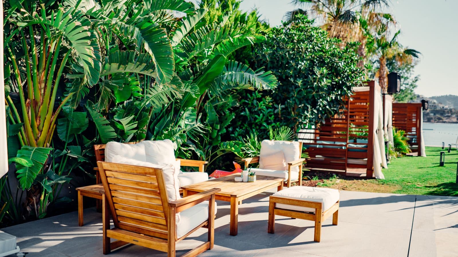 Modern seaside patio with large-format concrete slabs, teak lounge seating and lush tropical greenery overlooking the water