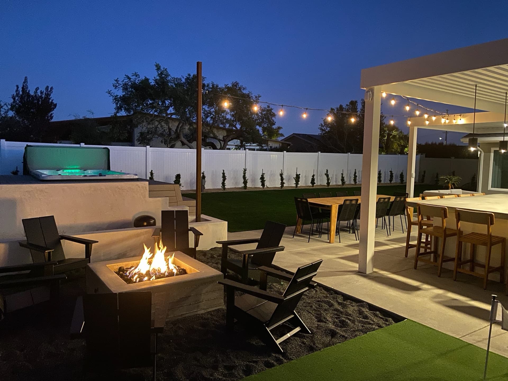 Resort patio with a fire pit, lit spa, and pergola at dusk, designed and built by Modern Yardz in Chula Vista, San Diego County