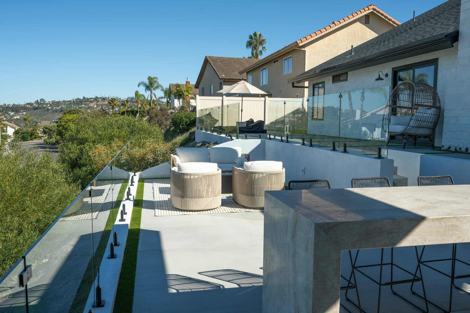Multi-level backyard with a fire lounge, turf joints, and glass railing by Modern Yardz in Carlsbad