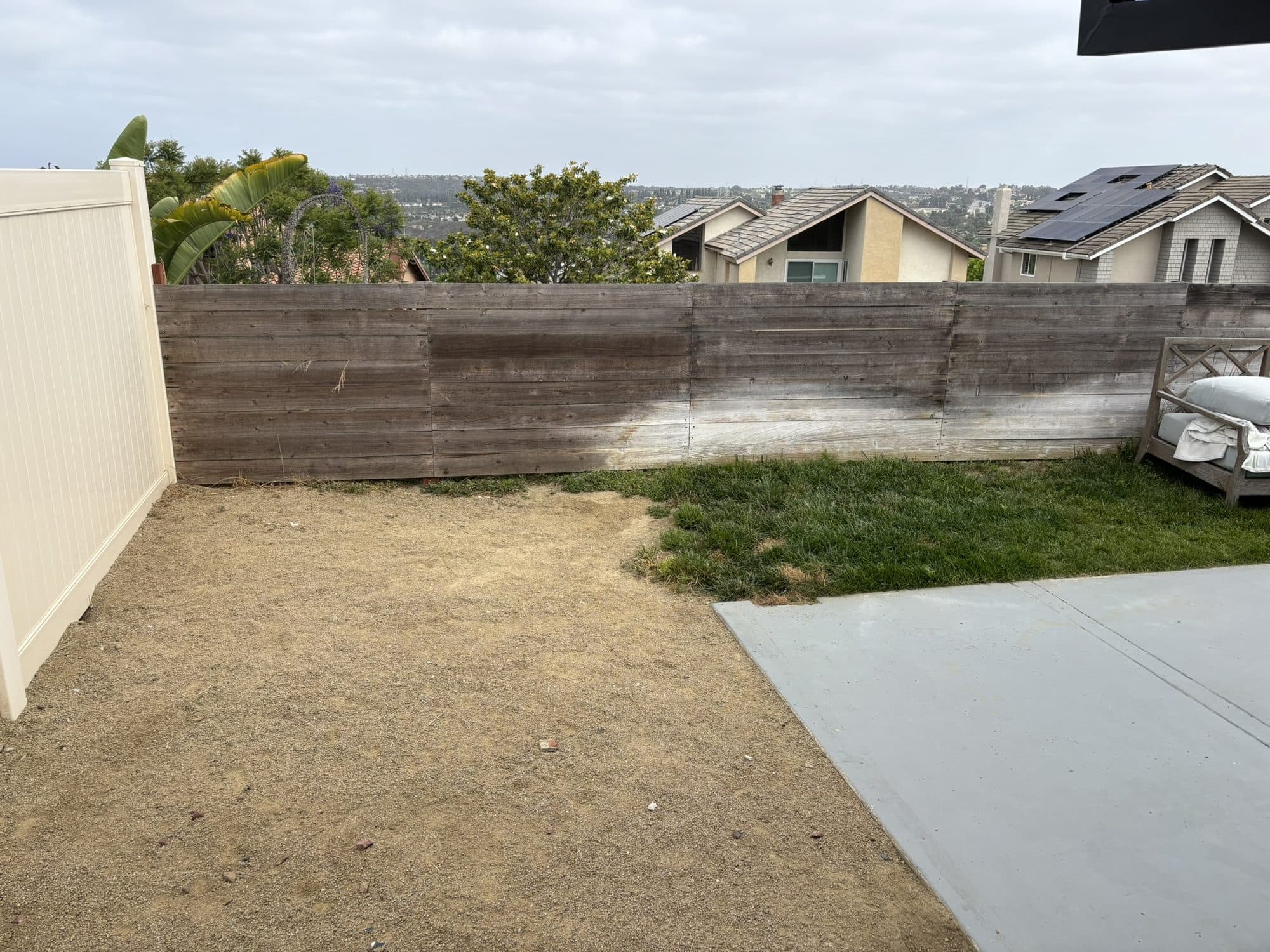 Before: the bare dirt backyard with an old wood retaining wall and vinyl fencing