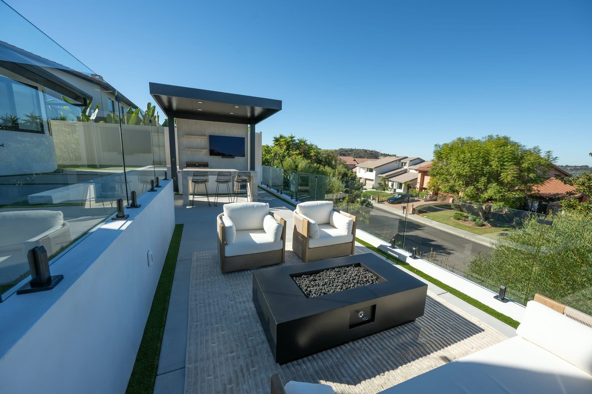 Multi-level Carlsbad backyard with a fire-pit lounge, frameless glass railings and an outdoor kitchen framing the ocean view