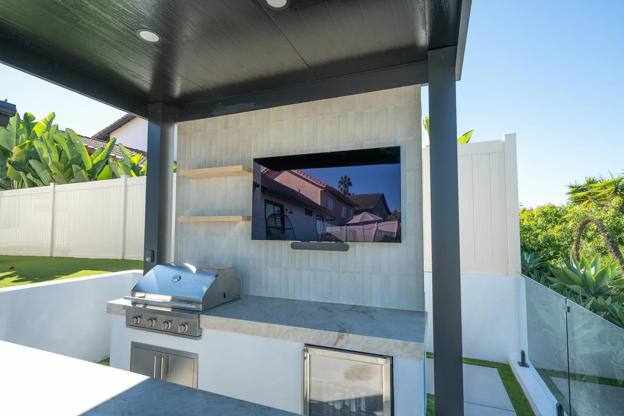 Outdoor kitchen with a built-in grill, integrated television on a tile feature wall, and a floating Taj Mahal quartzite bar in Carlsbad