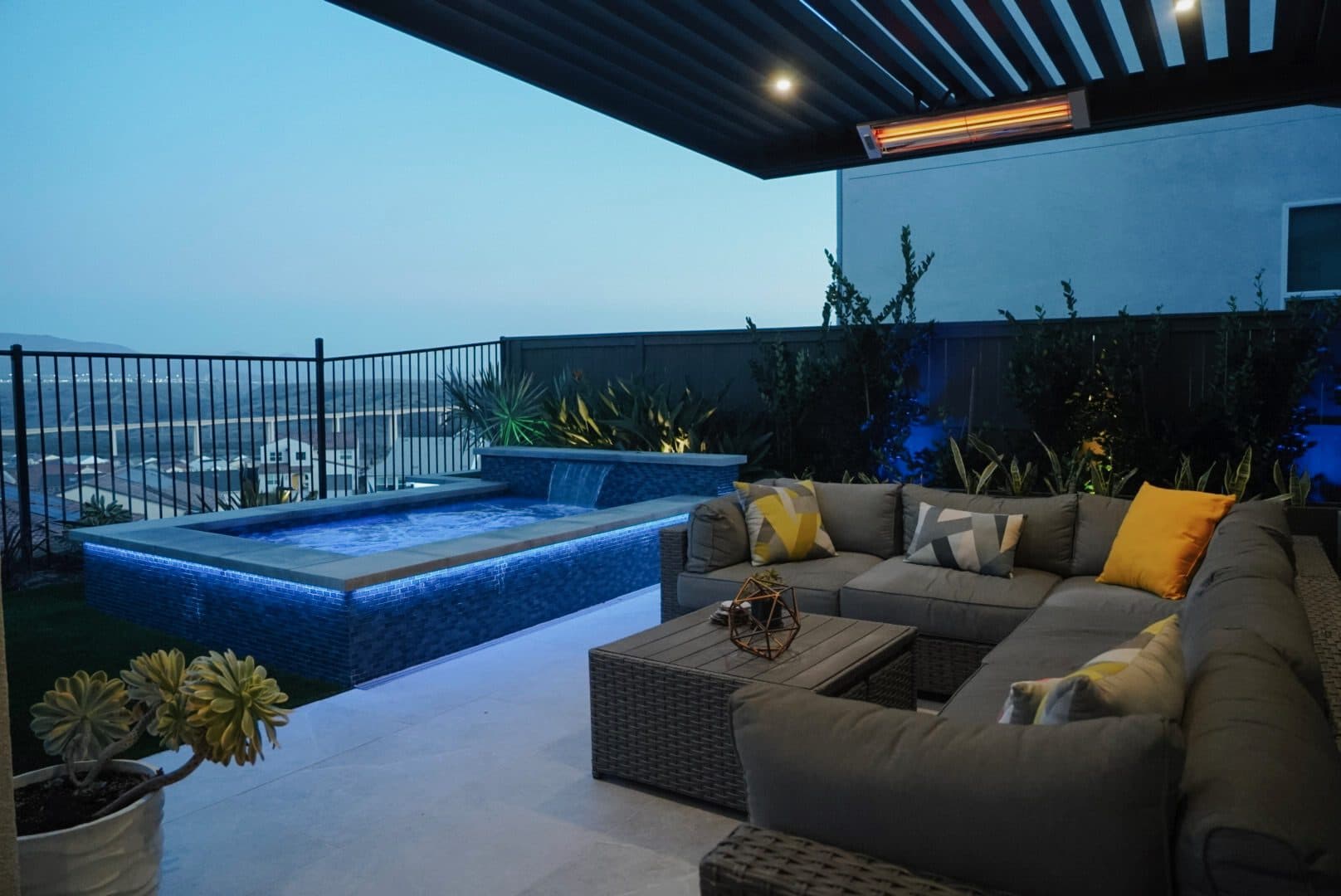 Patio lounge with a sectional beside a lit spool at dusk by Modern Yardz in Chula Vista