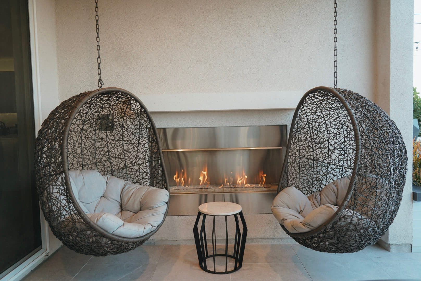 Hanging egg chairs beside a fireplace under the pergola
