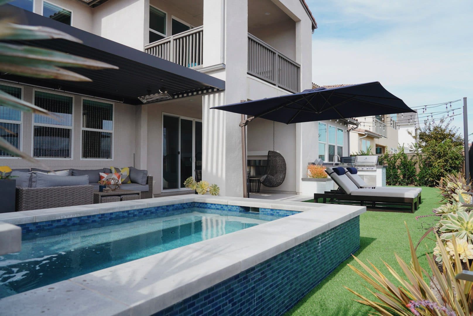 Backyard in Chula Vista with a blue glass-tile spool, cantilever pergola and outdoor kitchen