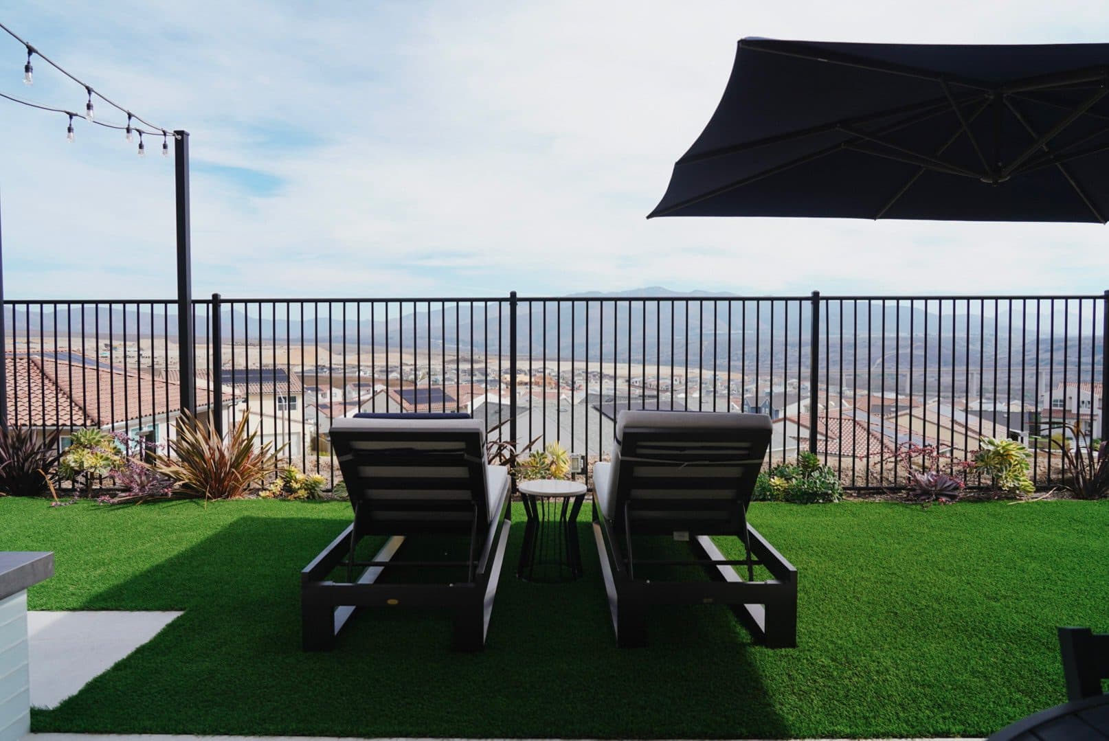Loungers on the artificial turf behind the black rail, cantilever umbrella open toward the valley