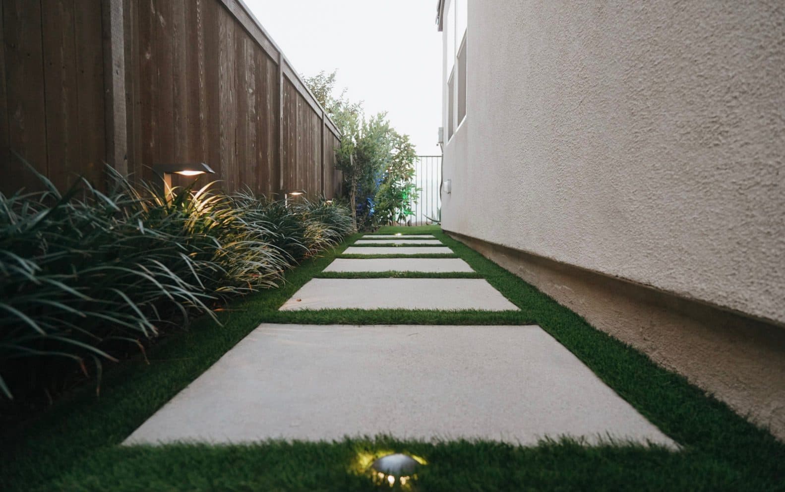 Side-yard path of concrete pads set in turf with path lights by Modern Yardz in Chula Vista