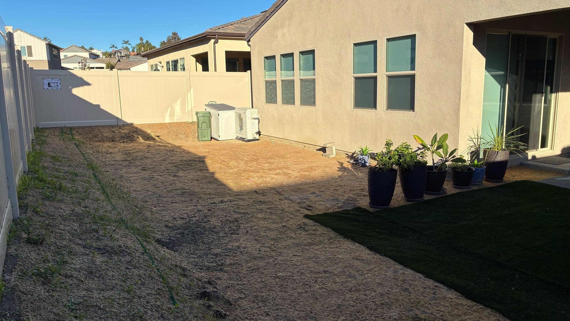 Before: the bare dirt backyard with exposed AC units against a vinyl fence