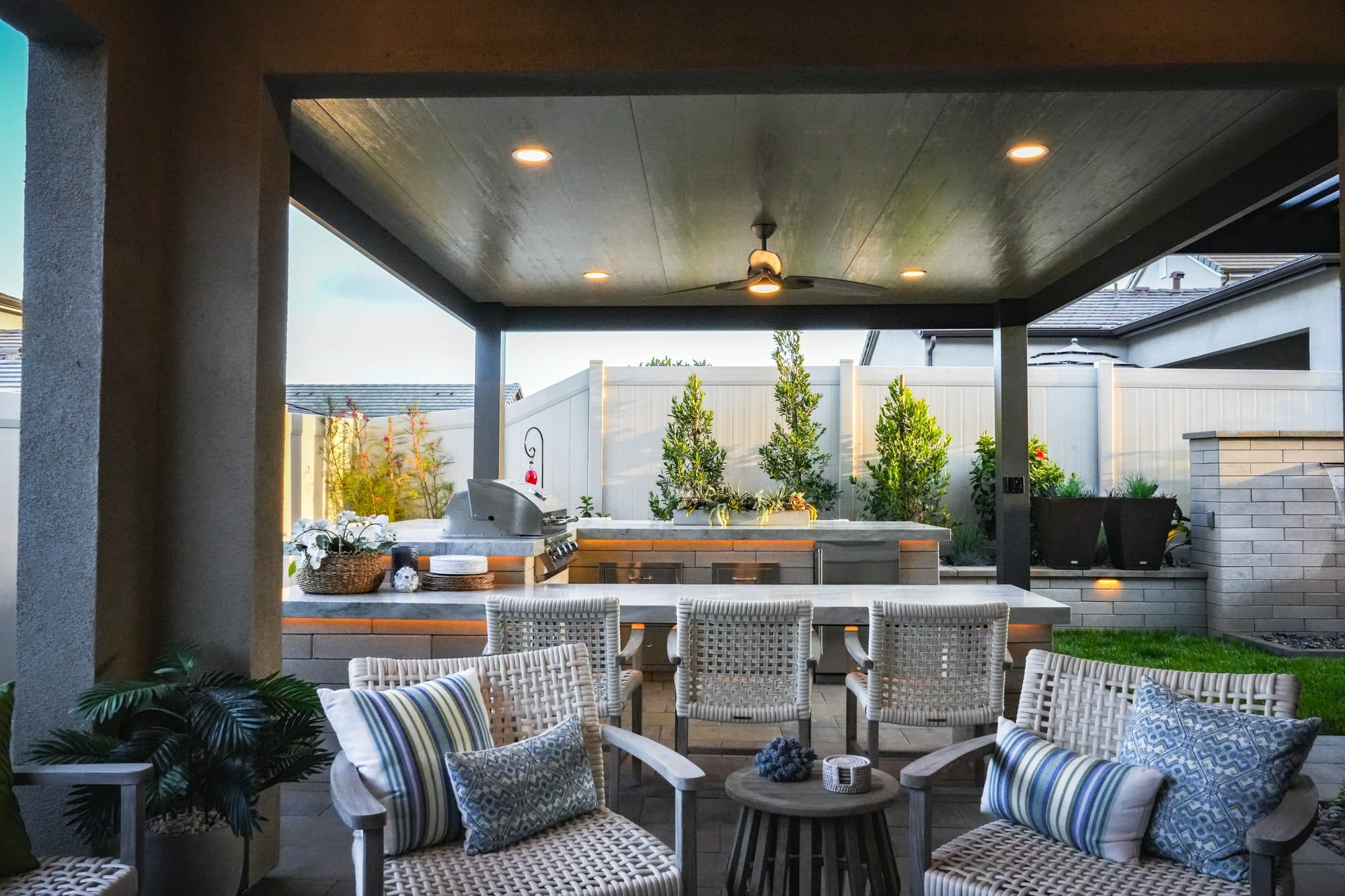 Covered living area with sectional seating and kitchen lit at dusk