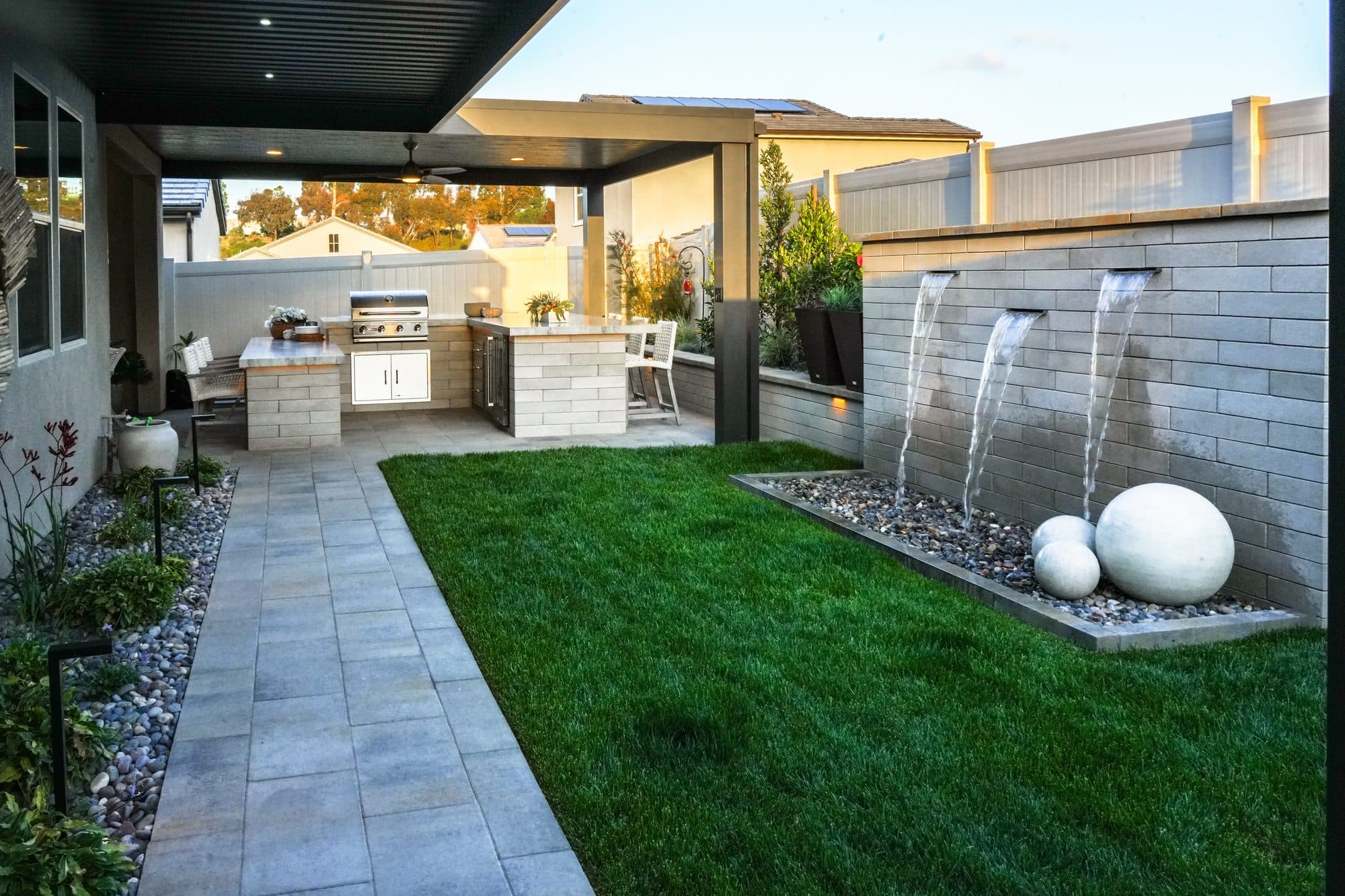Backyard in Rancho Bernardo with a covered outdoor kitchen, sod lawn and a Melville-block water feature with spheres