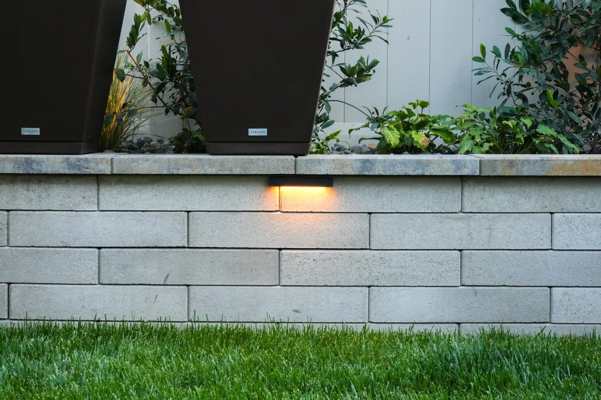 Block planter wall with built-in lights beside a lawn by Modern Yardz in Rancho Bernardo