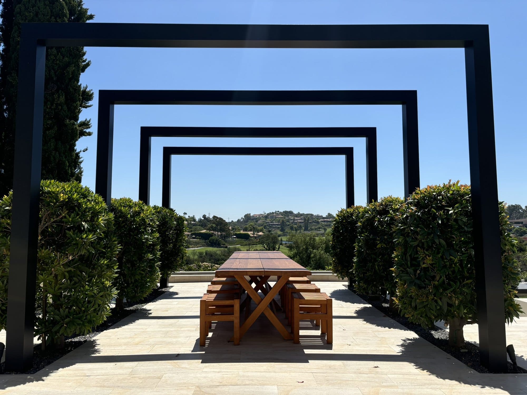 Four black steel arches framing a teak dining table with views over The Farms golf course in Rancho Santa Fe