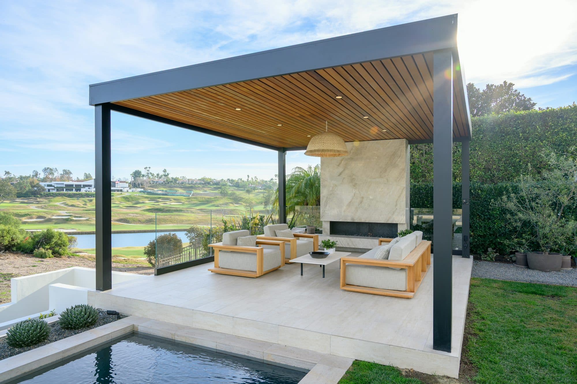 Black steel pergola with a cedar ceiling over a lounge beside a pool by Modern Yardz in Rancho Santa Fe