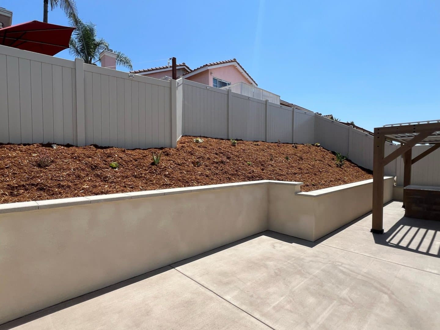 Backyard remodel with a new stucco retaining wall, concrete patio and pergola by Modern Yardz San Diego